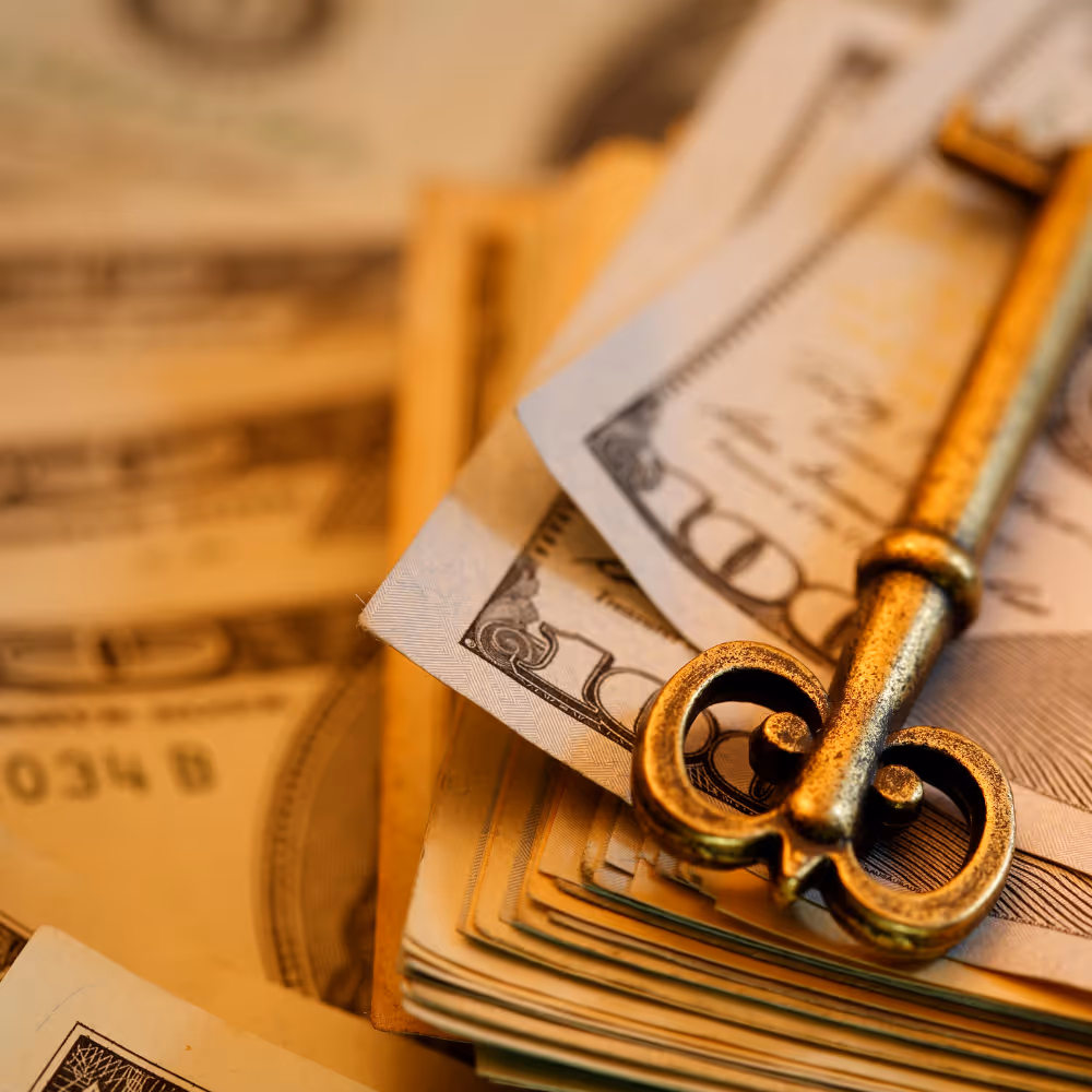 Close-up of an antique gold key resting on a stack of US dollar bills.
